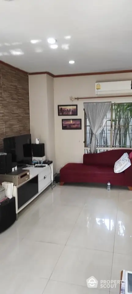 Spacious living room with glossy tiled flooring, modern lighting, and a large red sectional sofa, complemented by a stone accent wall.