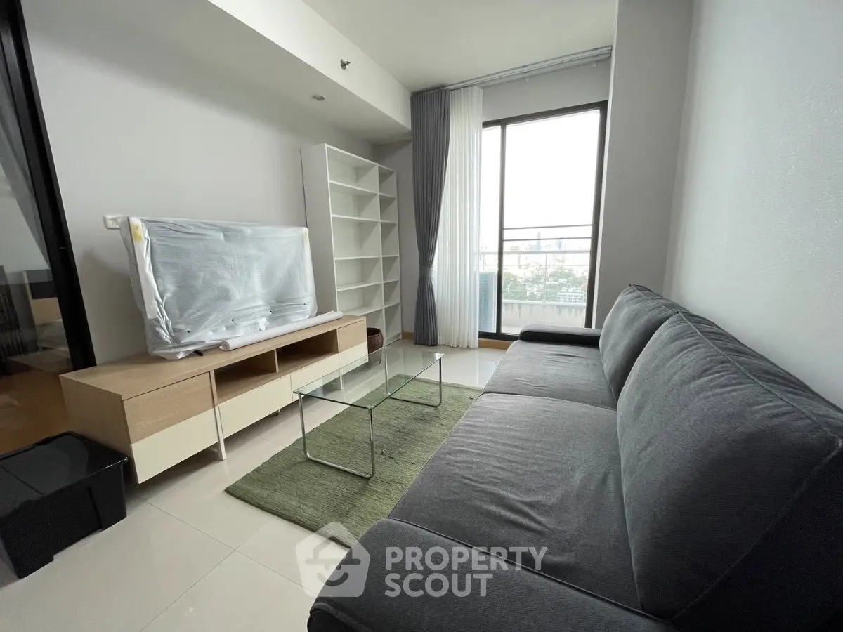 Modern living room with sleek furniture and large window offering natural light and city views.