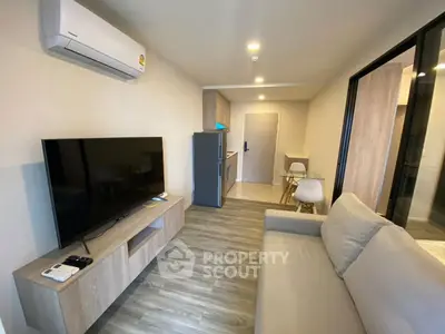 Modern living room with sleek furniture and open layout, featuring a large TV and air conditioning.