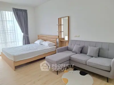 Spacious modern bedroom with cozy sofa and natural light, perfect for relaxation and comfort.