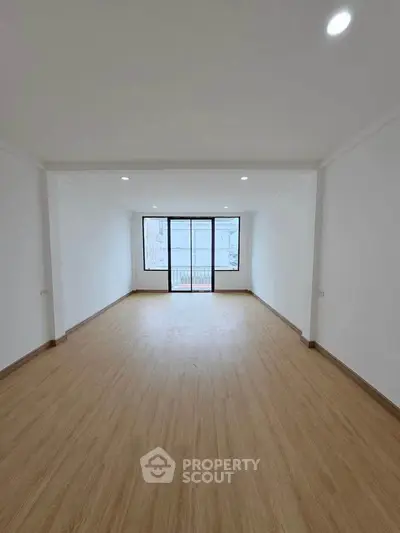 Spacious empty room with wooden flooring and large windows for natural light.