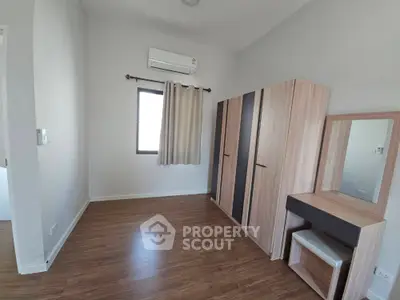 Spacious bedroom with modern wardrobe and vanity set, featuring sleek wooden flooring and natural light.