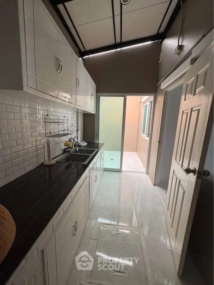 Modern kitchen with sleek black countertop and white cabinetry, featuring a closed layout and ample natural light.