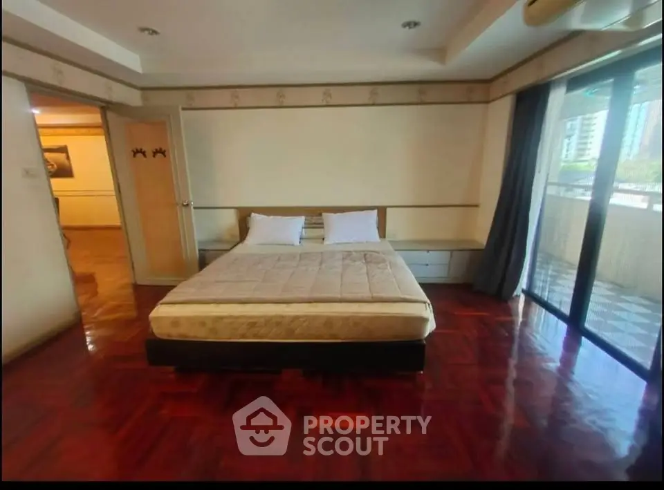 Spacious bedroom with wooden flooring and large window access to balcony in modern apartment.