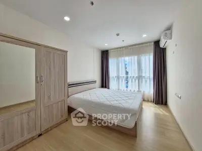 Modern bedroom with wooden flooring and large window, featuring a sleek wardrobe and comfortable bed.