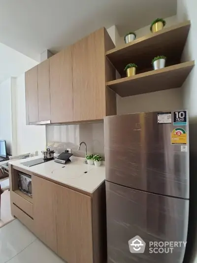 Modern kitchen with sleek wooden cabinets and stainless steel fridge in compact layout.