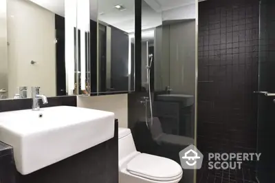 Sleek modern bathroom with a large mirror, chic black tiling, and a spacious glass-enclosed shower, exuding contemporary elegance and style.