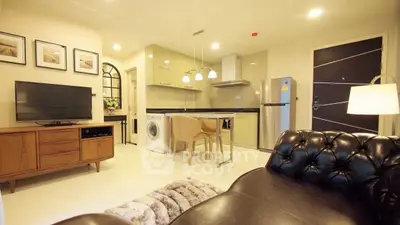 Modern living room with open kitchen, featuring leather sofa, TV, and appliances.