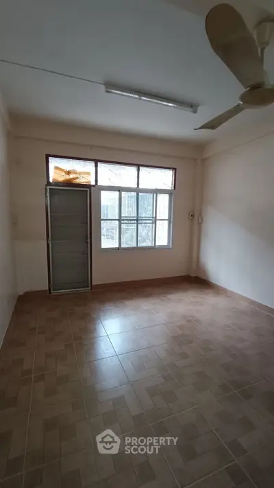 Spacious empty room with tiled floor and ceiling fan, ideal for customization.
