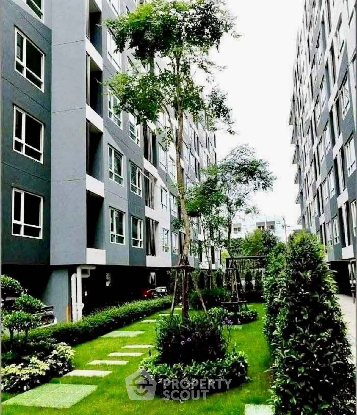 Modern apartment complex with lush green garden and pathway between buildings.