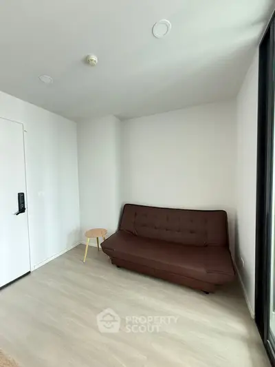 Modern minimalist living room with brown sofa and small wooden table, bright natural light.