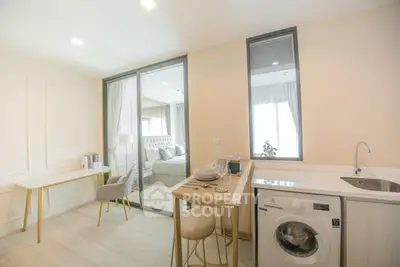 Modern apartment interior with open kitchen and washing machine, featuring elegant dining area and cozy bedroom view.