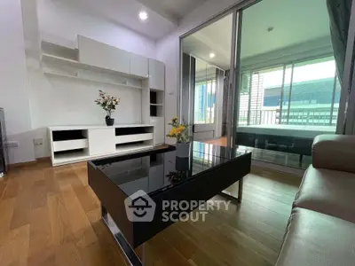 Modern living room with sleek furniture and glass partition leading to a bedroom, featuring wooden flooring.