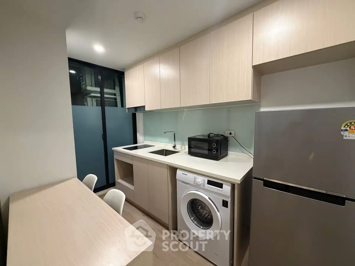 Modern kitchen with sleek cabinetry, washing machine, and stainless steel fridge in compact layout.