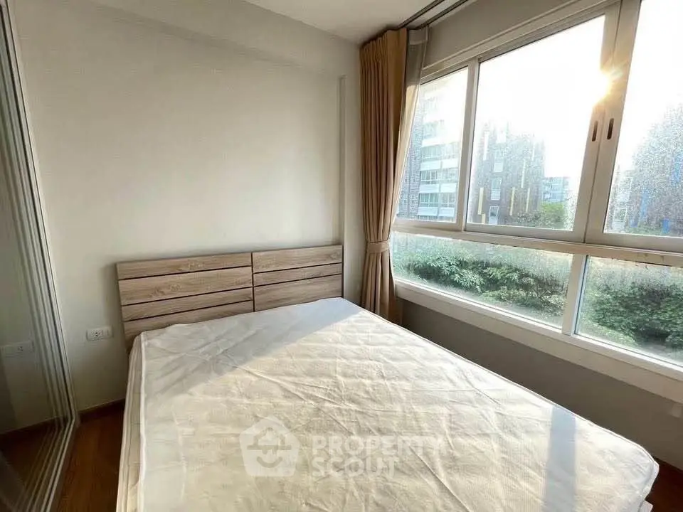 Bright bedroom with large windows and wooden headboard, offering a serene view of greenery outside.