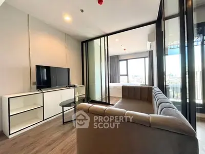 Modern living room with sleek glass doors and city view, featuring a cozy sofa and entertainment unit.