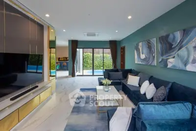 Luxurious living room with modern decor and pool view, featuring plush blue sofa and large TV.