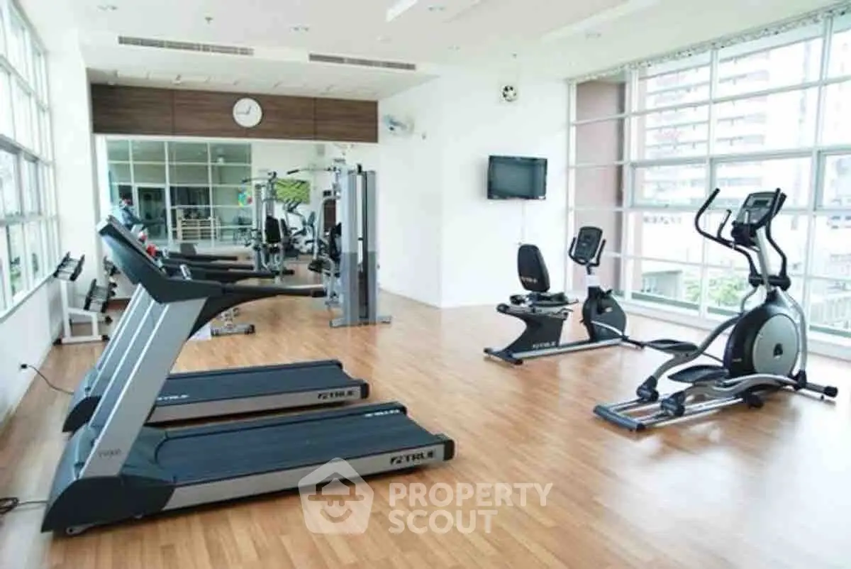 Spacious gym with modern fitness equipment and large windows in a residential building.