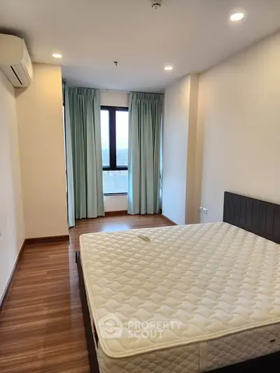 Spacious bedroom with large window and wooden flooring in modern apartment.