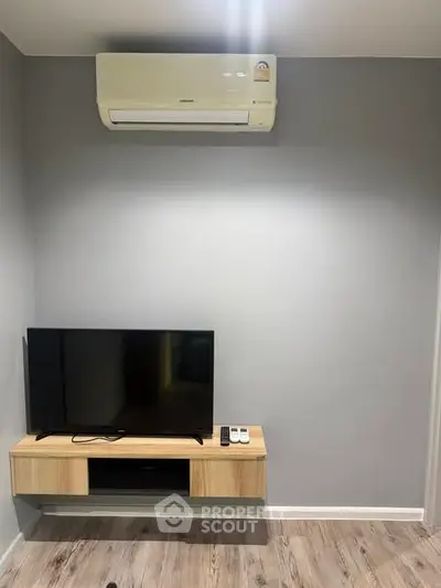 Modern living room with mounted TV and air conditioning unit, featuring sleek wooden flooring.