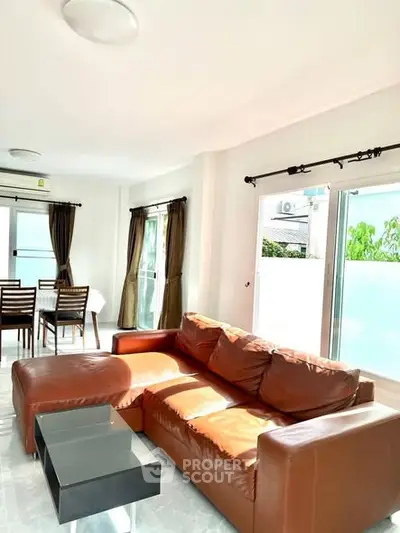 Spacious living room with leather sofa and dining area, abundant natural light.