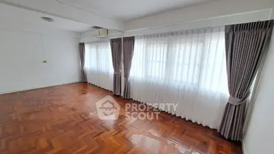 Spacious empty room with elegant parquet flooring and large windows with curtains.