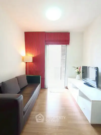 Cozy living room with modern sofa and TV unit, featuring bright red curtains and natural light.