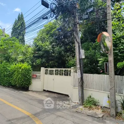Charming residential entrance with lush greenery and secure gate in a peaceful neighborhood.
