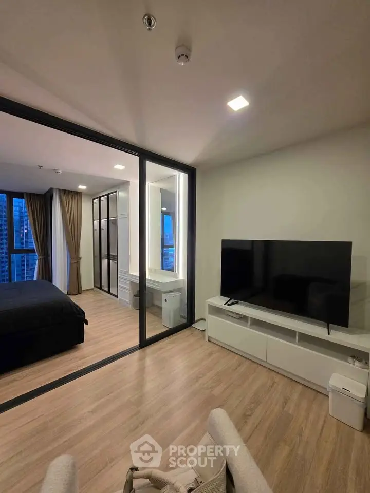 Modern living room with sleek TV setup and view into stylish bedroom with floor-to-ceiling windows.