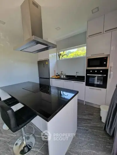 Modern kitchen with sleek black countertops, built-in oven, and stylish bar seating.