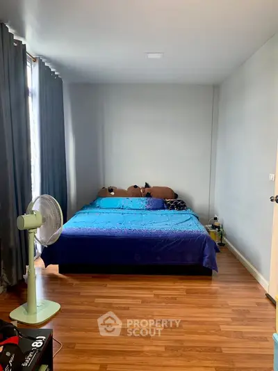 Spacious bedroom with wooden flooring and large window, featuring a cozy bed and modern decor.