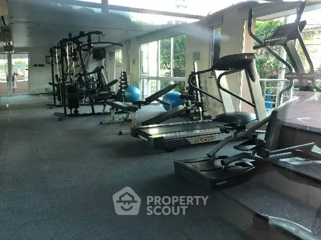 Spacious gym with modern equipment and large windows offering natural light.