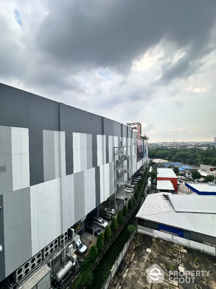 Modern industrial building with expansive rooftop and urban surroundings under cloudy sky.