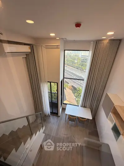 Modern loft-style living room with high ceilings and large windows offering city views.