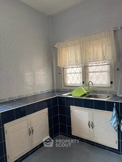 Charming kitchen with blue tile accents and natural light, featuring a double sink and ample storage space.