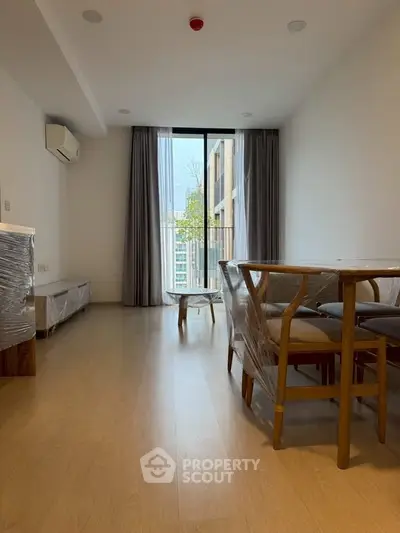 Modern living room with wooden flooring and dining set, featuring large windows and natural light.