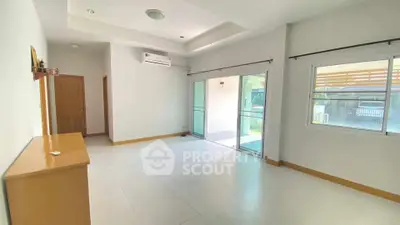 Spacious living room with large windows and sliding glass doors leading to a balcony, featuring modern air conditioning.