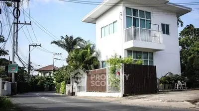 Modern two-story white house with balcony and lush greenery on a quiet street corner.