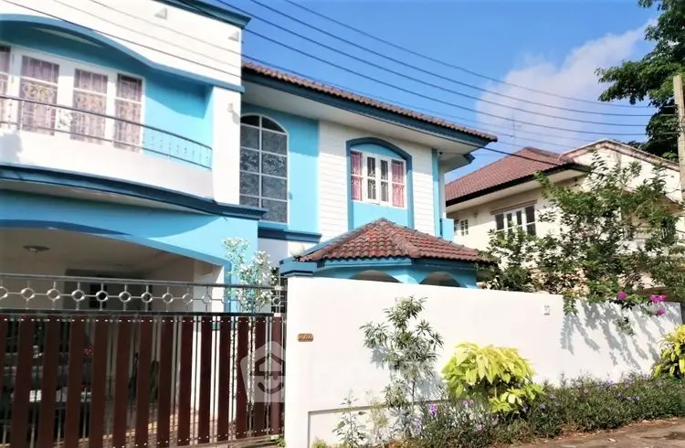 Charming two-story blue house with tiled roof and lush garden in a serene neighborhood.