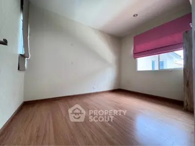 Spacious empty room with wooden flooring and large window, perfect for customization.
