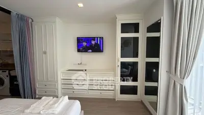 Modern bedroom with built-in wardrobe and TV, featuring elegant white cabinetry and natural light.