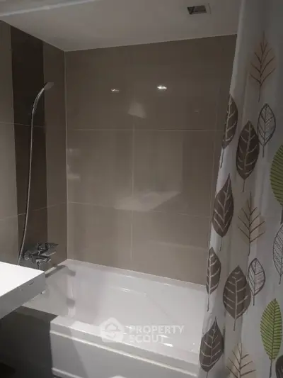 Modern bathroom with sleek tiles and bathtub, featuring a stylish leaf-patterned shower curtain.