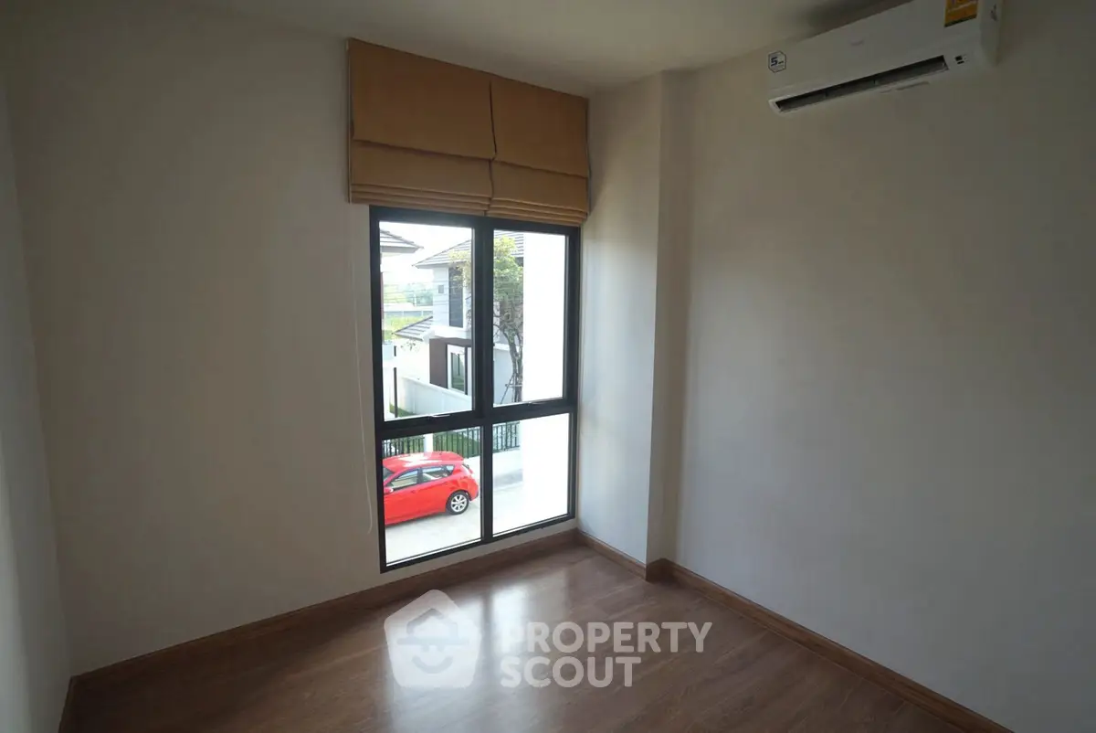 Bright empty room with wooden flooring and large window, perfect for customization.