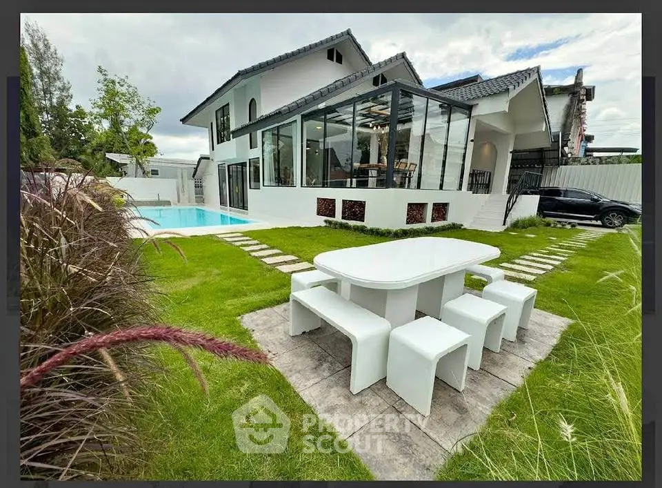 Luxurious modern home with glass extension and pool, featuring elegant outdoor dining area.