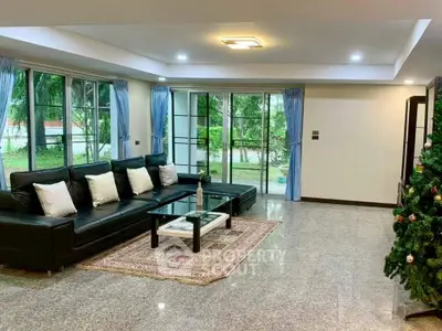 Spacious living room with modern decor and large windows overlooking lush greenery.