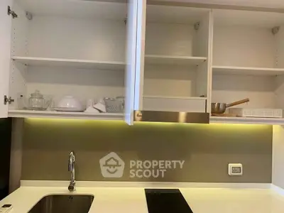 Modern kitchen with sleek cabinetry and under-cabinet lighting, featuring an electric cooktop and stainless steel sink.