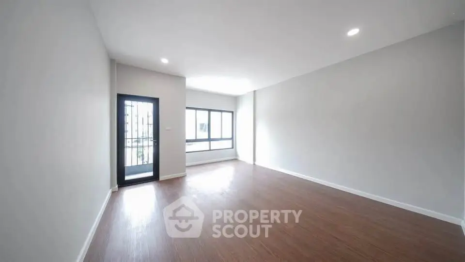 Spacious empty living room with large windows and wooden flooring, perfect for customization.
