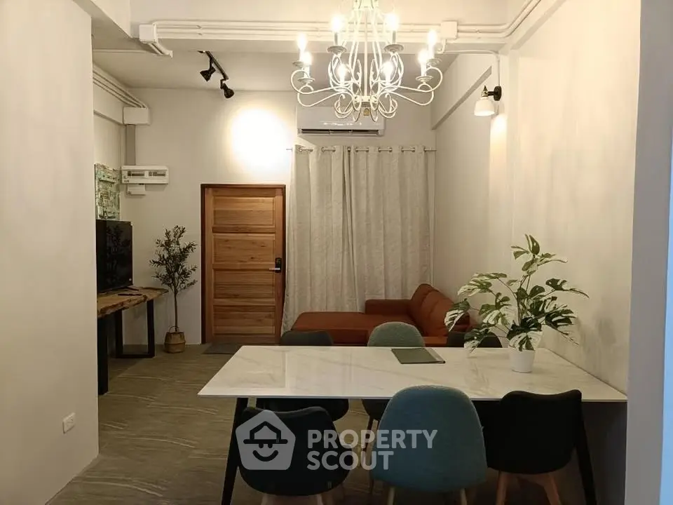 Modern living room with elegant chandelier, cozy sofa, and stylish dining area in open layout.