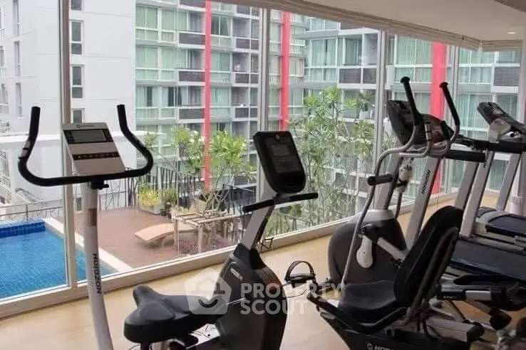 Modern gym with exercise bikes and pool view in luxury apartment complex.