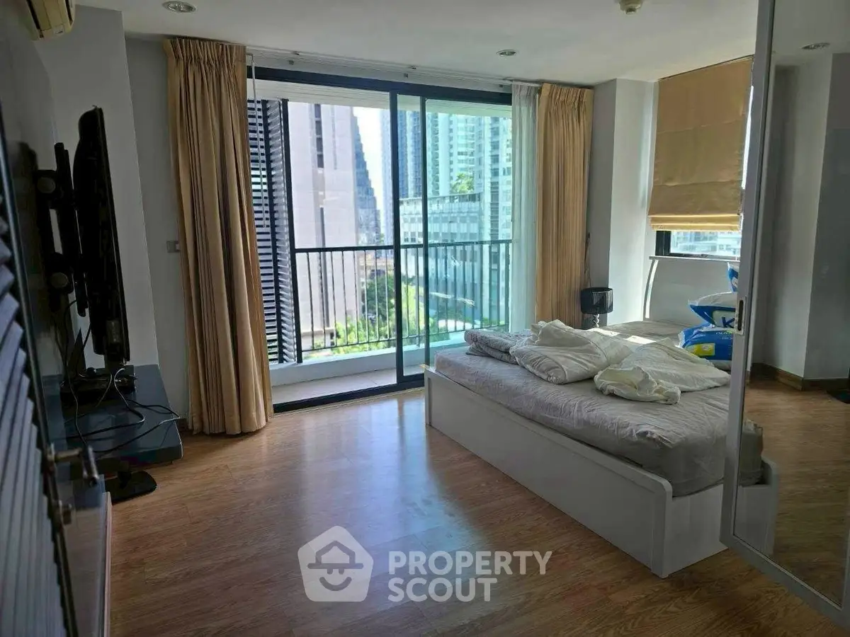 Spacious bedroom with balcony and city view, featuring modern decor and natural light.